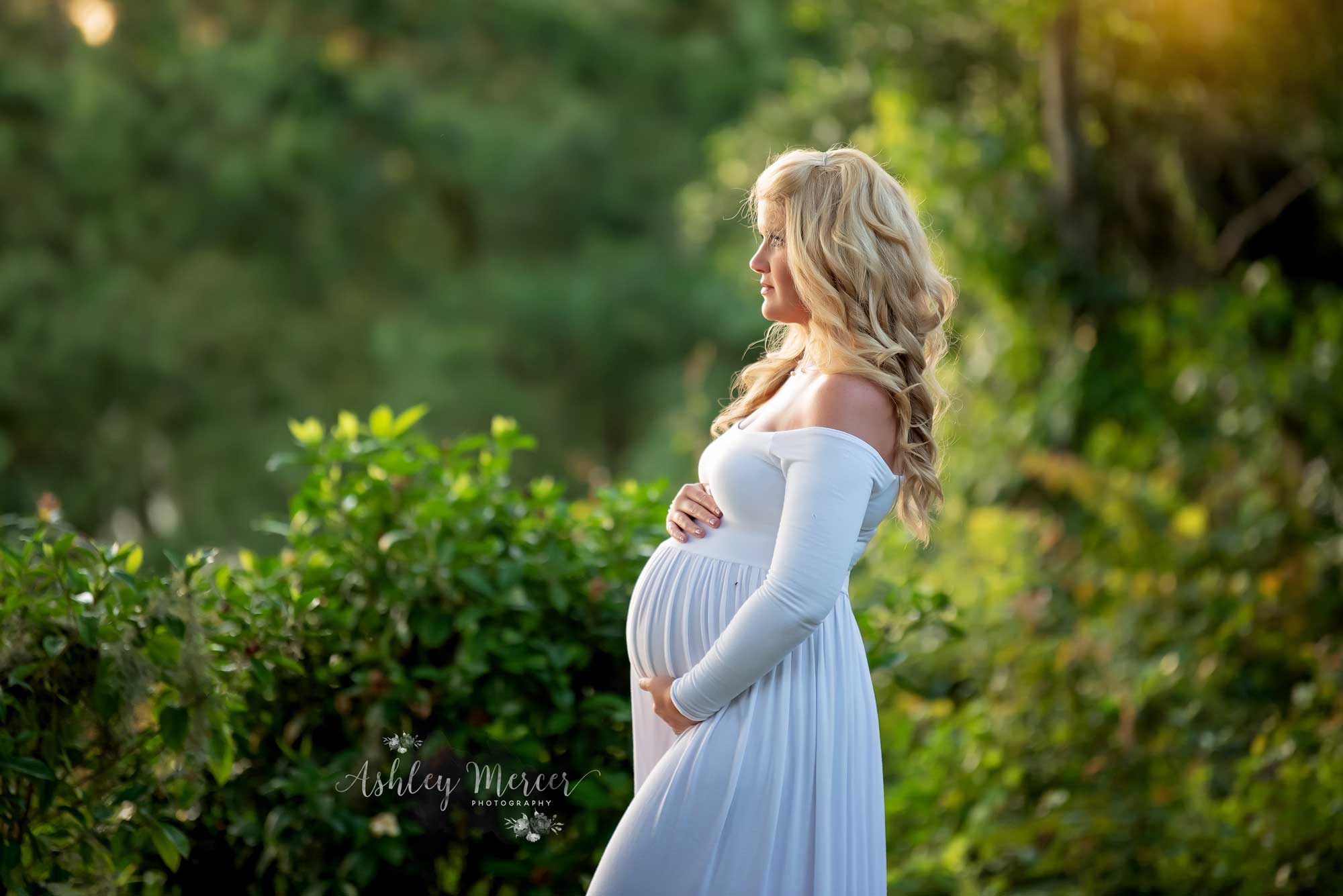 A pregnant mom is holding her belly while looking off into the distance in a lush green garden