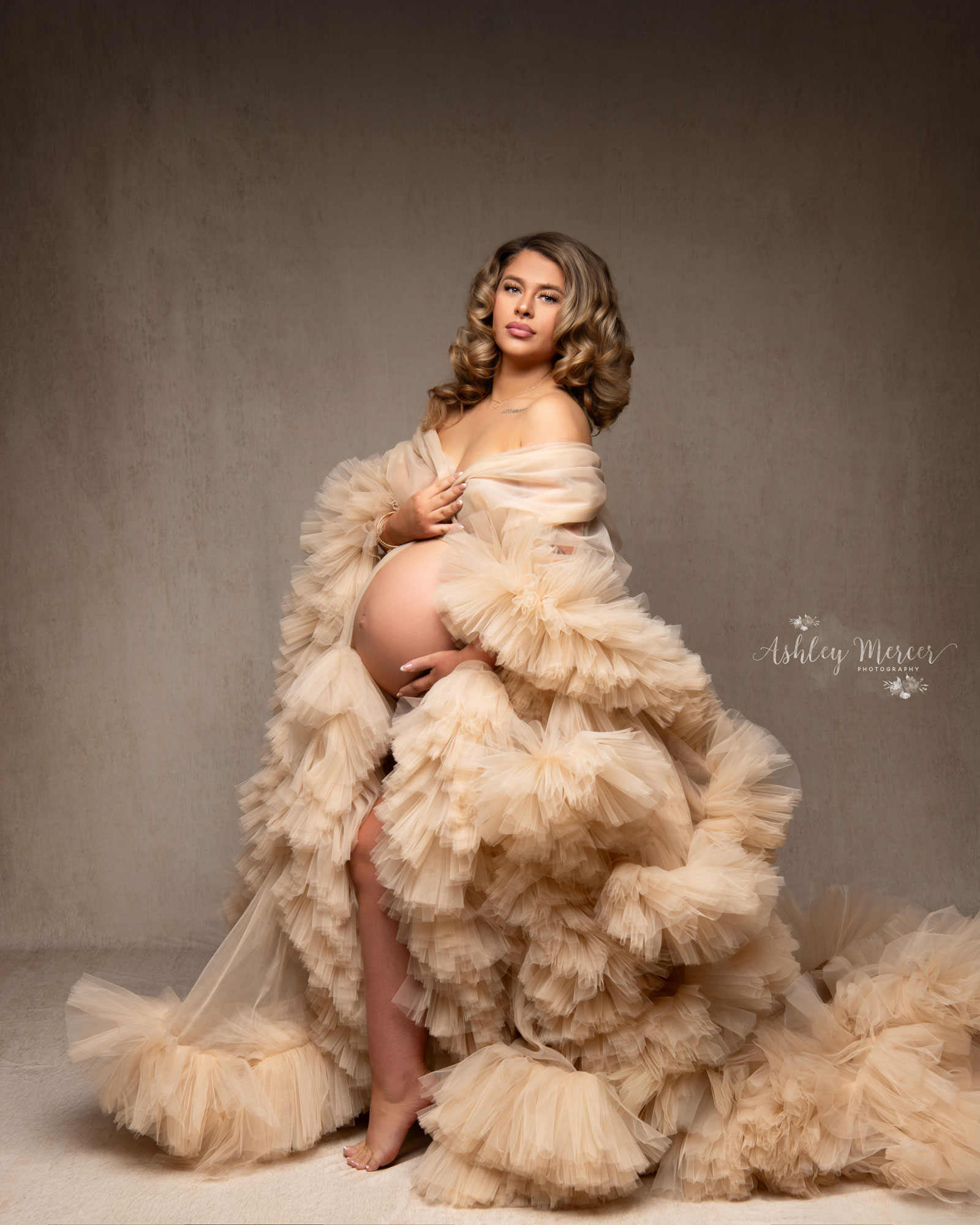 A sexy, sultry maternity session where the pregnant woman is wearing a cream robe, draped off one shoulder and showing off her bare belly.