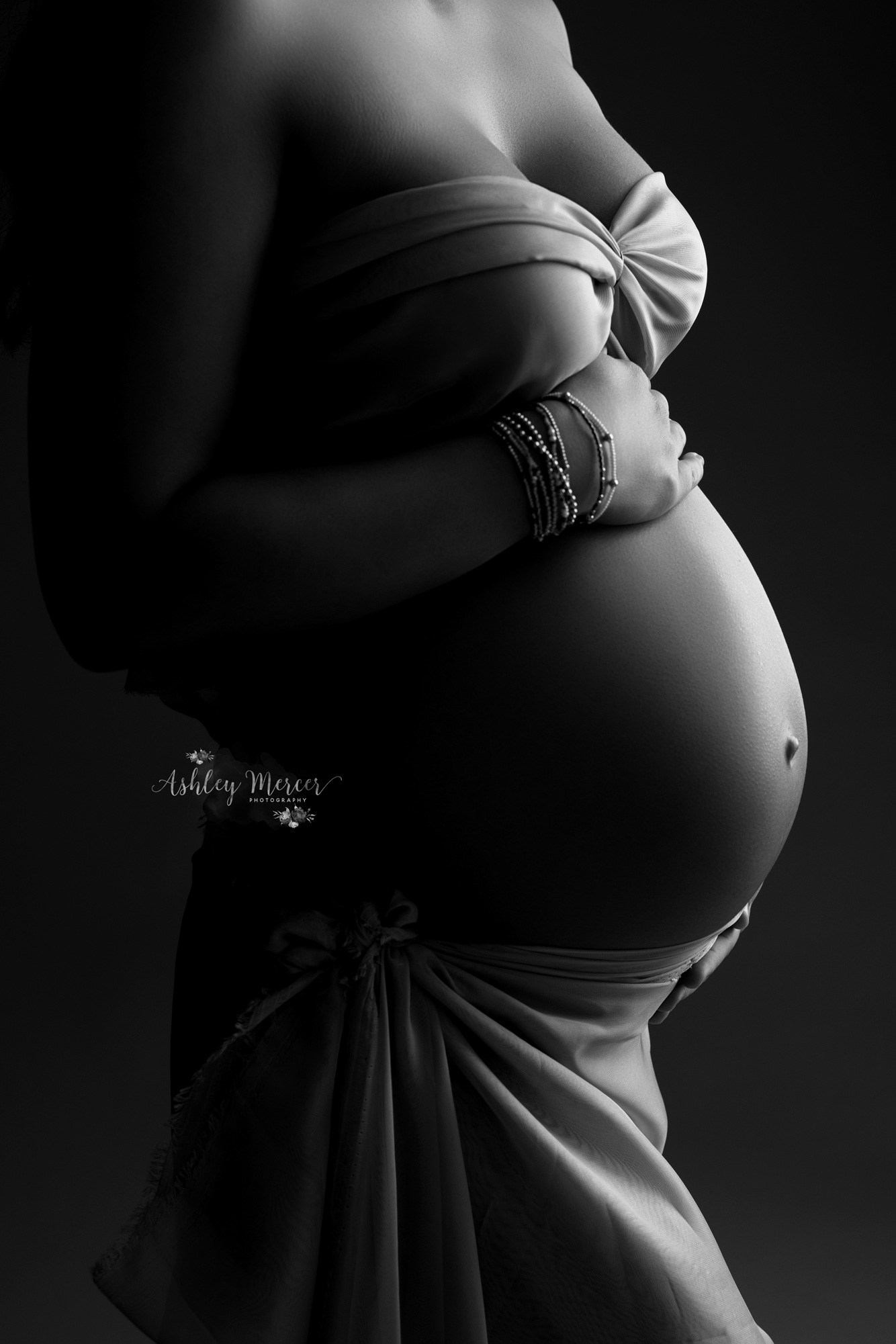 A close up, silhouette of a pregnant moms, belly in black and white with light on just one side.