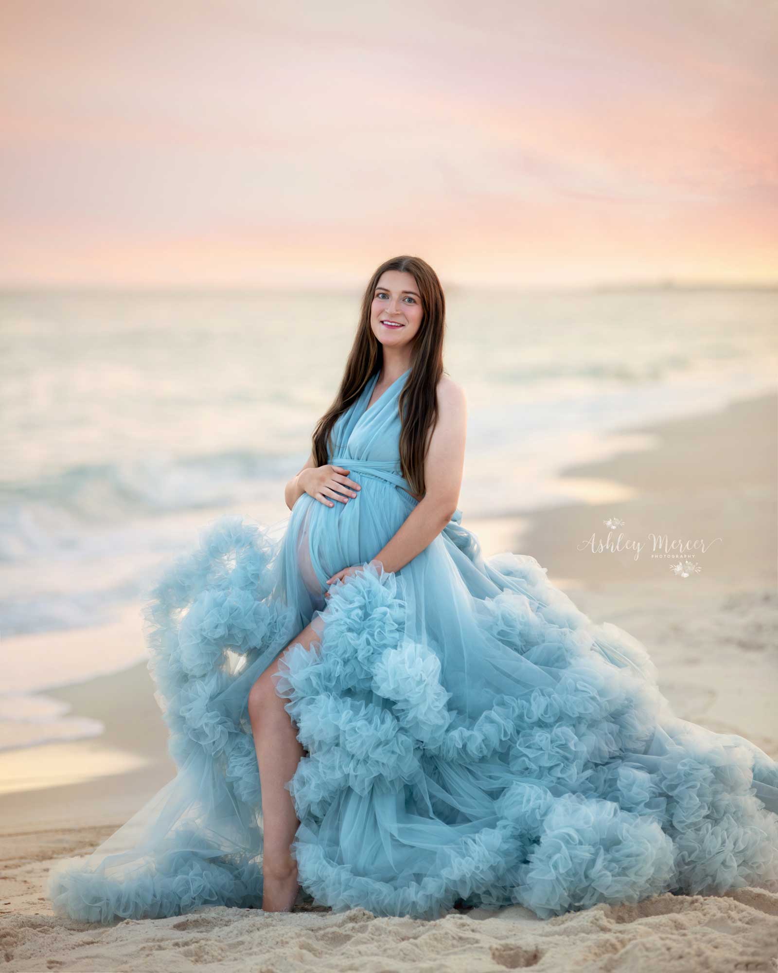 A pregnant mom to be at Orange Beach Alabama wearing a blue, tulle gown during a stunning pastel sunset.