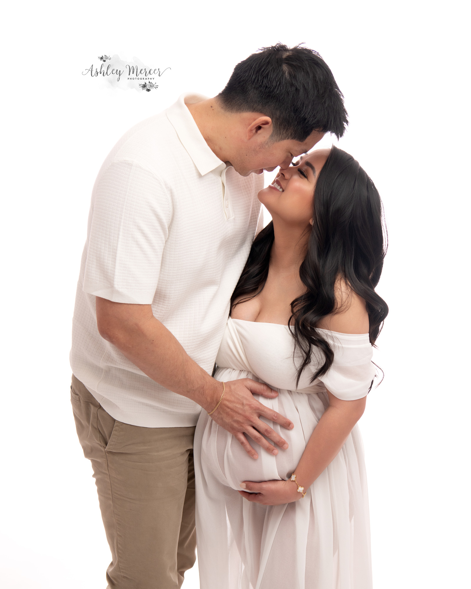 Pregnant couple lovingly embracing each other while the father places a hand on the moms belly.