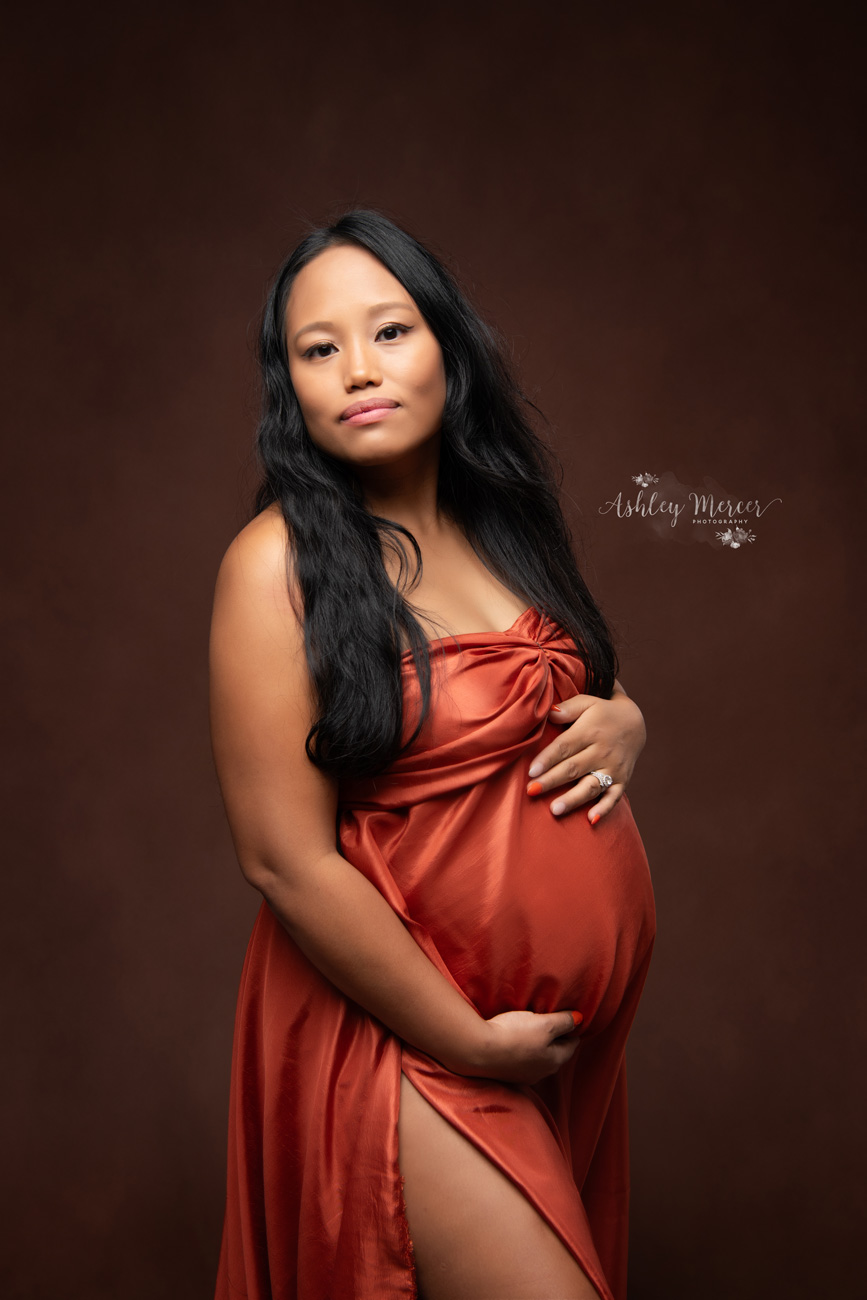 Stunning maternity photo of a mom in a burnt orange gown with a dark brown background