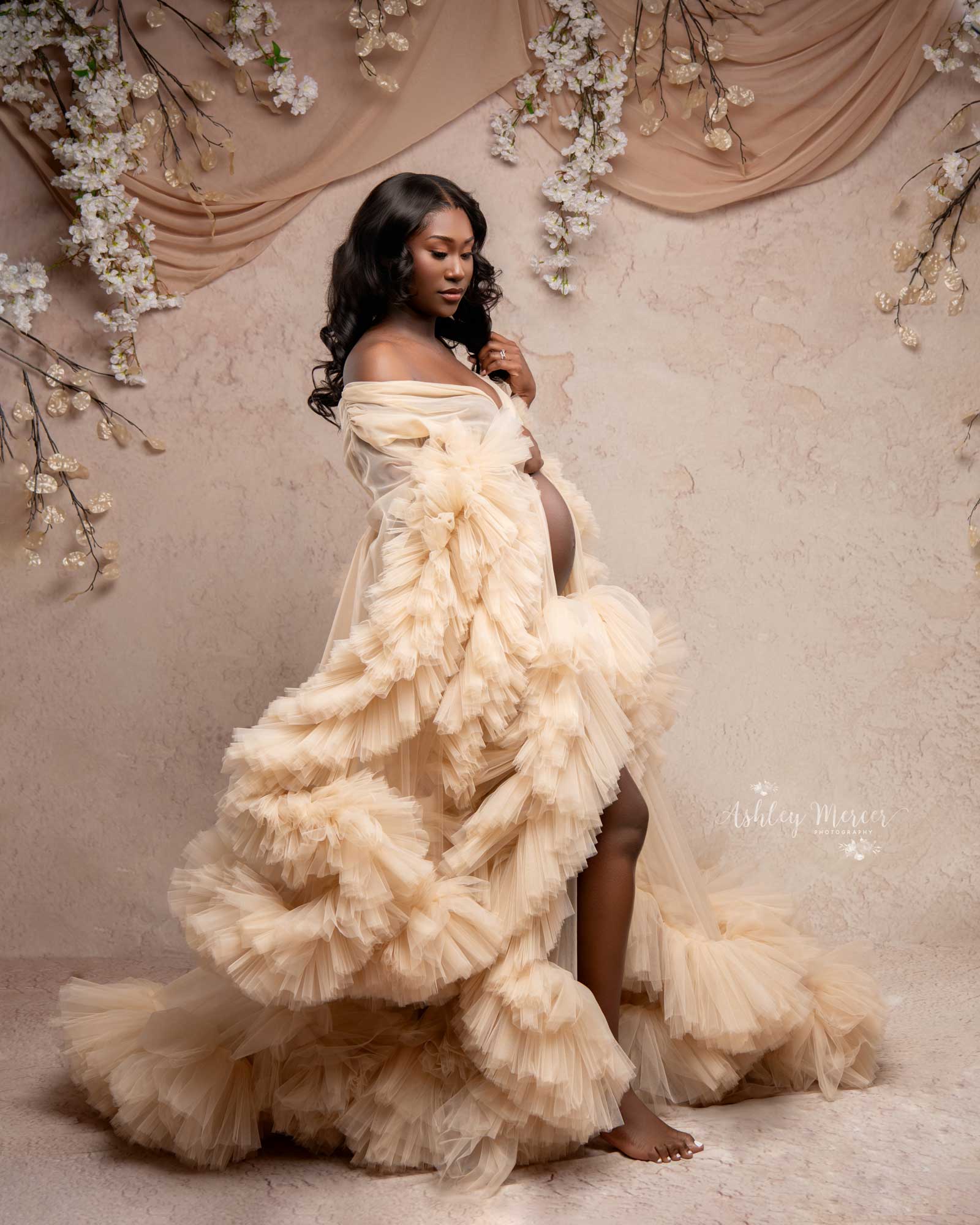 A romantic feeling maternity session with the mom wearing a cream robe that shows off her belly. She is loving looking down at her belly.