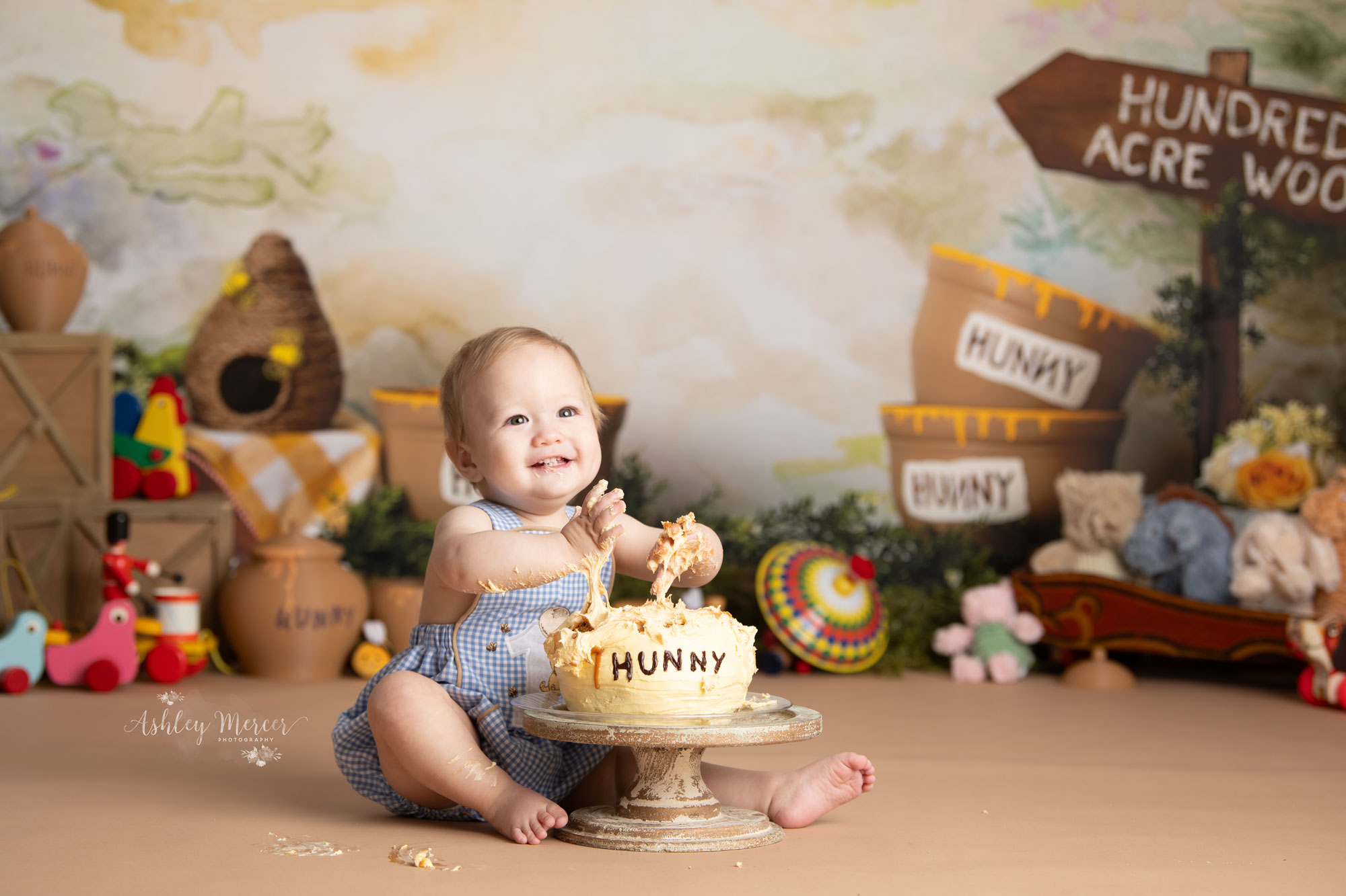 Baby boy smashing his hands into his first birthday cake shaped like a honey pot from Winnie the Pooh bear